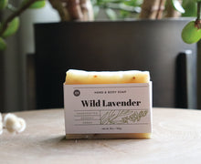 Load image into Gallery viewer, Wild Lavender hand and body soap bar on a table near a plant. handcrafted, organic, vegan. Olive Seed