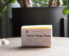 Load image into Gallery viewer, Sweet Ylang Ylang soap bar sitting on stand with plant. Olive Seed