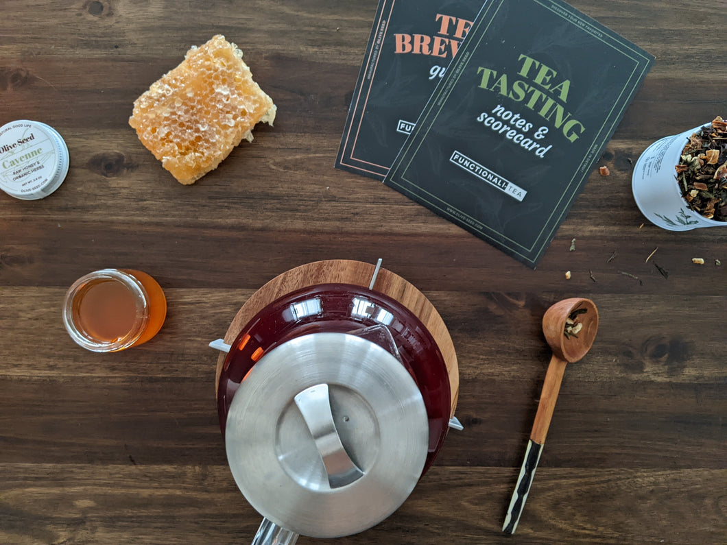cayenne honey on a table with honeycomb, loose leaf tea in a tin, olive wood teaspoon and tasting cards