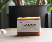 Load image into Gallery viewer, Frank &amp; Myrrh 5 oz. hand and body soap bar on a stand with a plant. handcrafted, all natural, vegan. Olive Seed
